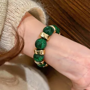 Close-up detail of dark green resin bead and gold metal spacer fashion bracelet worn on wrist.