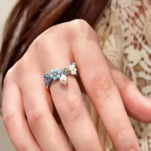 Detaillierte Nahaufnahme eines zarten Perlenblumenrings mit blauen und weißen Perlen und Anhänger.