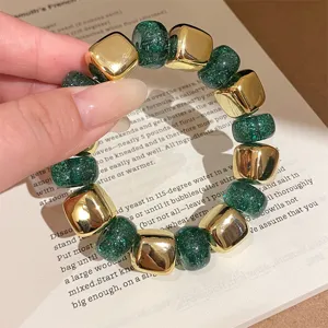 Close-up detail of green resin and gold cube bracelet, elegant fashion jewelry accessory.