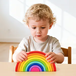 Image principale d'un adorable tout-petit jouant avec un jouet empilable arc-en-ciel en bois sur table.
