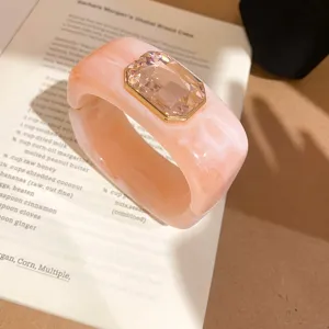 Primer plano de pulsera brazalete de resina marmoleada rosa con gran cristal de talla esmeralda.
