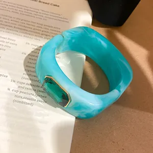 Vista detallada de un brazalete de resina turquesa con incrustación de cristal verde.