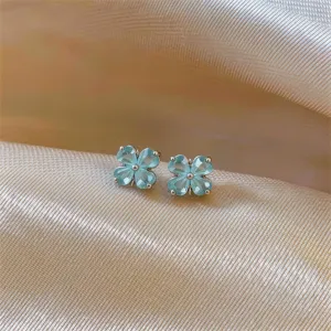 Detailed close-up of light blue four-petal flower zircon stud earrings on satin background.