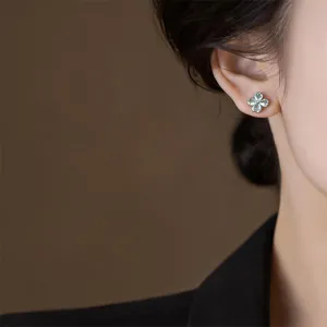 Close-up detail shot of exquisite four-petal flower zirconia stud earrings worn on ear.