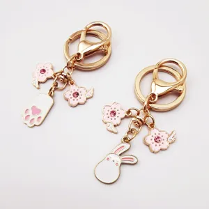 Close-up detail of cute alloy keychain with pink enamel cherry blossom and cartoon rabbit charms.