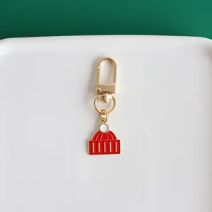 Metal hat pendant keychain detail shot, golden hardware with red enamel decor for bags and keys.