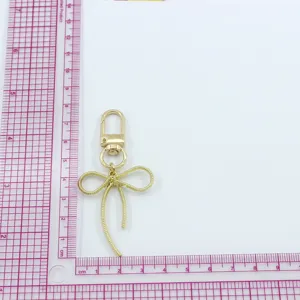 Close-up gold metal bow keychain charm detail with delicate hollow design and practical lobster clasp.