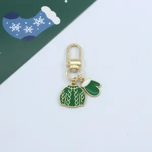 Detailed shot of Christmas metal keychain with green sweater and mitten enamel pendants.