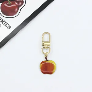 Close-up of the cute apple pendant keychain detail, showing shiny gold clasp and enamel.
