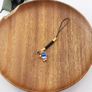 Starry astronaut phone charm detail shot, featuring black braided strap and cute space pendant.