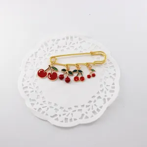 Encantador broche de imperdible dorado con bonitos colgantes de cerezas rojas y hojas verdes.