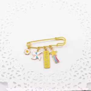Detail shot of a cute gold-tone safety pin brooch with enamel charms, daisy and blessing tag.