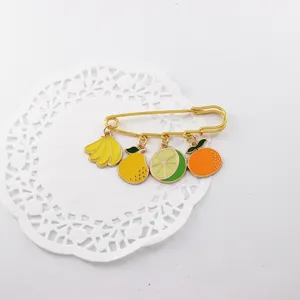 Detalle de un bonito broche de imperdible con colgantes de frutas de esmalte muy colorido.
