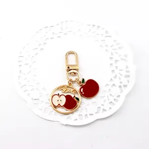 Close-up of a cute gold-tone alloy apple keychain charm with red and white enamel fruit details.
