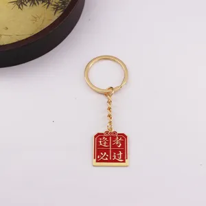 Porte-clés en métal doré avec pendentif en émail rouge pour le succès aux examens.
