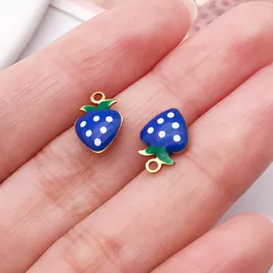 Close-up detail of blue strawberry enamel charm with white polka dots and gold plated edge.