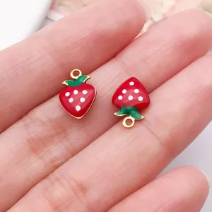 Close-up detail of cute red enamel strawberry pendants with gold-plated edges for DIY jewelry.