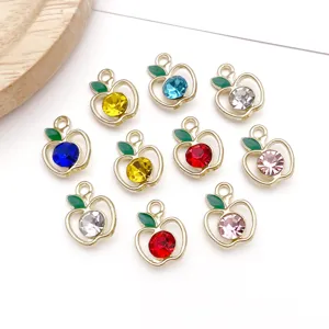 Close-up of DIY alloy apple pendants with sparkling rhinestones and green enamel leaf details.