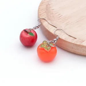 Close-up detail shot of cute resin apple and persimmon fruit earrings on wood plate.