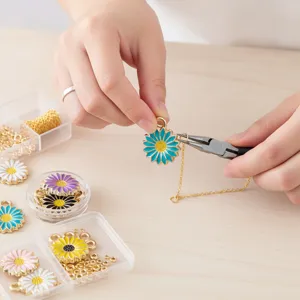 Close-up detail of DIY enamel daisy flower charms with pliers and gold chains for crafting.
