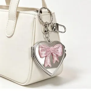 Detail shot of heart-shaped mirror keychain with pink glitter bow charm hanging on a bag.