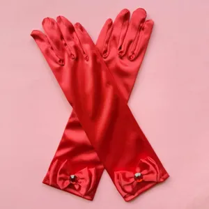 Primer plano de guantes de satén rojo para niños con lazo elegante y estrás brillante.