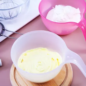 Closeup of plastic mixing bowls with buttercream frosting, whisk, and strainer for baking.