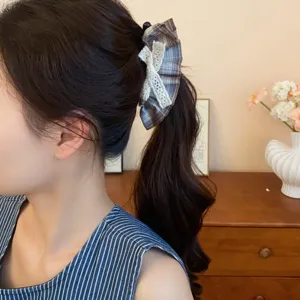 Detail view of brown plaid hair scrunchie with white lace bow for ponytail styling.