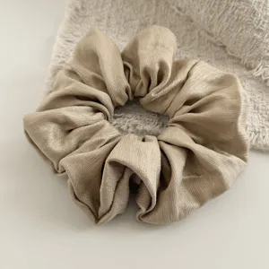 Gedetailleerd zicht op een glanzende beige haarscrunchie met een zachte geplooide textuur.