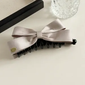Satijnen strik haarklauw clip detail, elegante champagne haarspeld met zwarte kunststof tanden.
