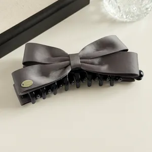 Gedetailleerde close-up van donkergrijze satijnen strik haarspeld, elegant verticaal haaraccessoire.