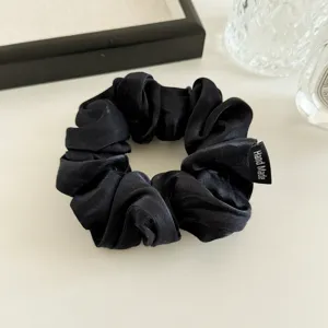 Black satin fabric hair scrunchie detail shot, elegant shiny pony tail holder accessory.