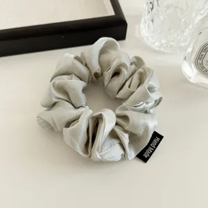 Detailed close-up of an elegant pearl-sheen satin hair scrunchie featuring a handmade label.