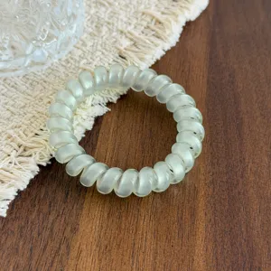 Close-up view of a transparent light green telephone cord hair tie on a wooden tabletop.
