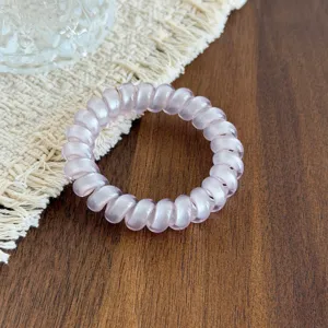 Close-up detail of a light pink glossy telephone cord hair tie on a wooden surface.