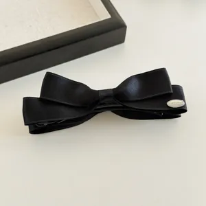 Detailansicht der schwarzen Satin Schleife Bananen Haarklammer mit eleganter Plakette.
