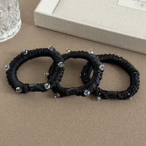 Detail shot of black pleated satin hair scrunchies decorated with shiny crystals and beads.