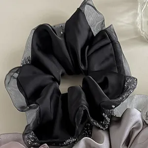 Close-up of black satin scrunchie with sheer organza ruffles and sparkling rhinestones.