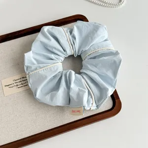 Light blue fabric hair scrunchie with white piping detail, elegant hair accessory close up.