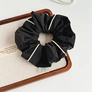 Korean minimalist piped fabric hair scrunchie close-up detail, elegant black with white edge.
