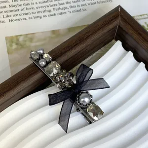Detailed close-up of the elegant rhinestone pearl and black bow hair clip on a chic white tray.