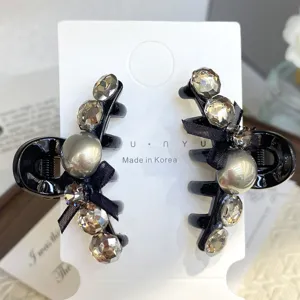 Detailed close-up of a pair of black hair claw clips decorated with rhinestones and bows.