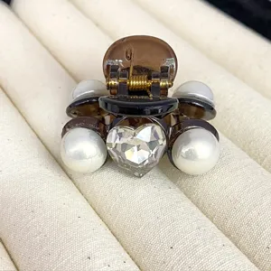 Close-up detail of small brown resin hair claw clip featuring sparkling heart crystal and pearls.