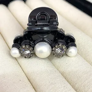 Close-up detail of black mini hair claw clip featuring elegant pearl and rhinestone flower decor.