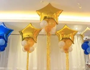 Party balloon decoration detail showing gold star foil balloons and tinsel curtain backdrop setup.