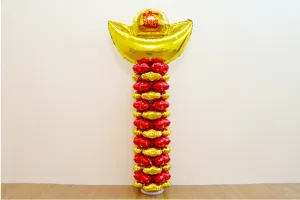 Detail view of festive balloon pillar decoration featuring a golden ingot top and balloons.