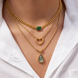 Close-up of layered gold necklaces with emerald green stone, twisted heart and teardrop pendant.