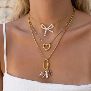 Close-up detail of multi-layer gold chain necklace featuring pearl bow and pendant charms.