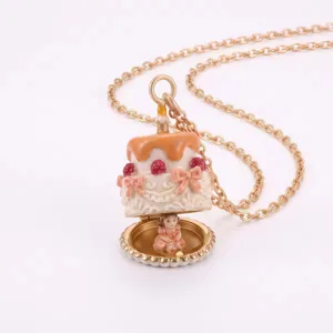 Collier chaîne doré avec pendentif gâteau en émail ouvrant, nœuds et baies rouges.