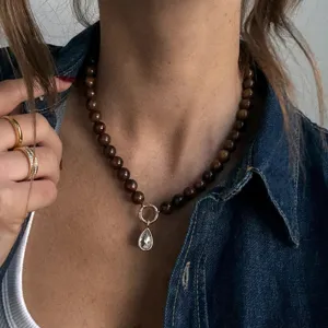 Detailopname van de handgemaakte kralenketting met bruine ronde kralen en een druppelkristal.